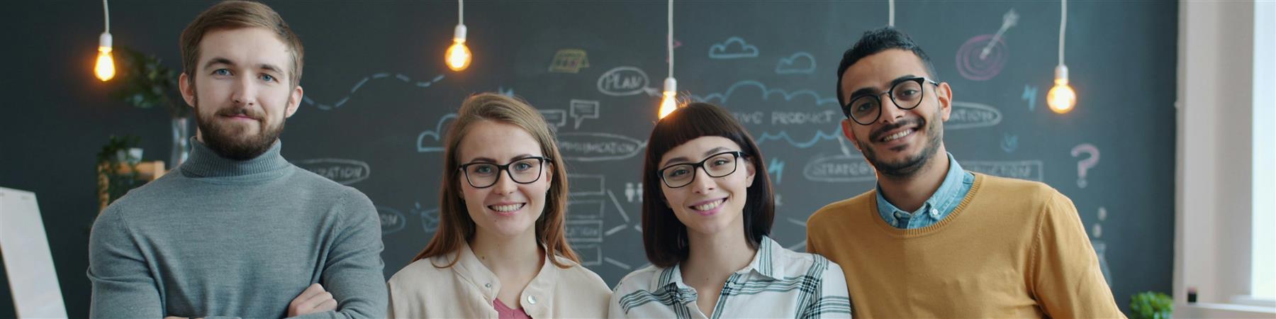 Equipo de cuatro personas sonriendo en una oficina moderna con una pizarra de ideas detras